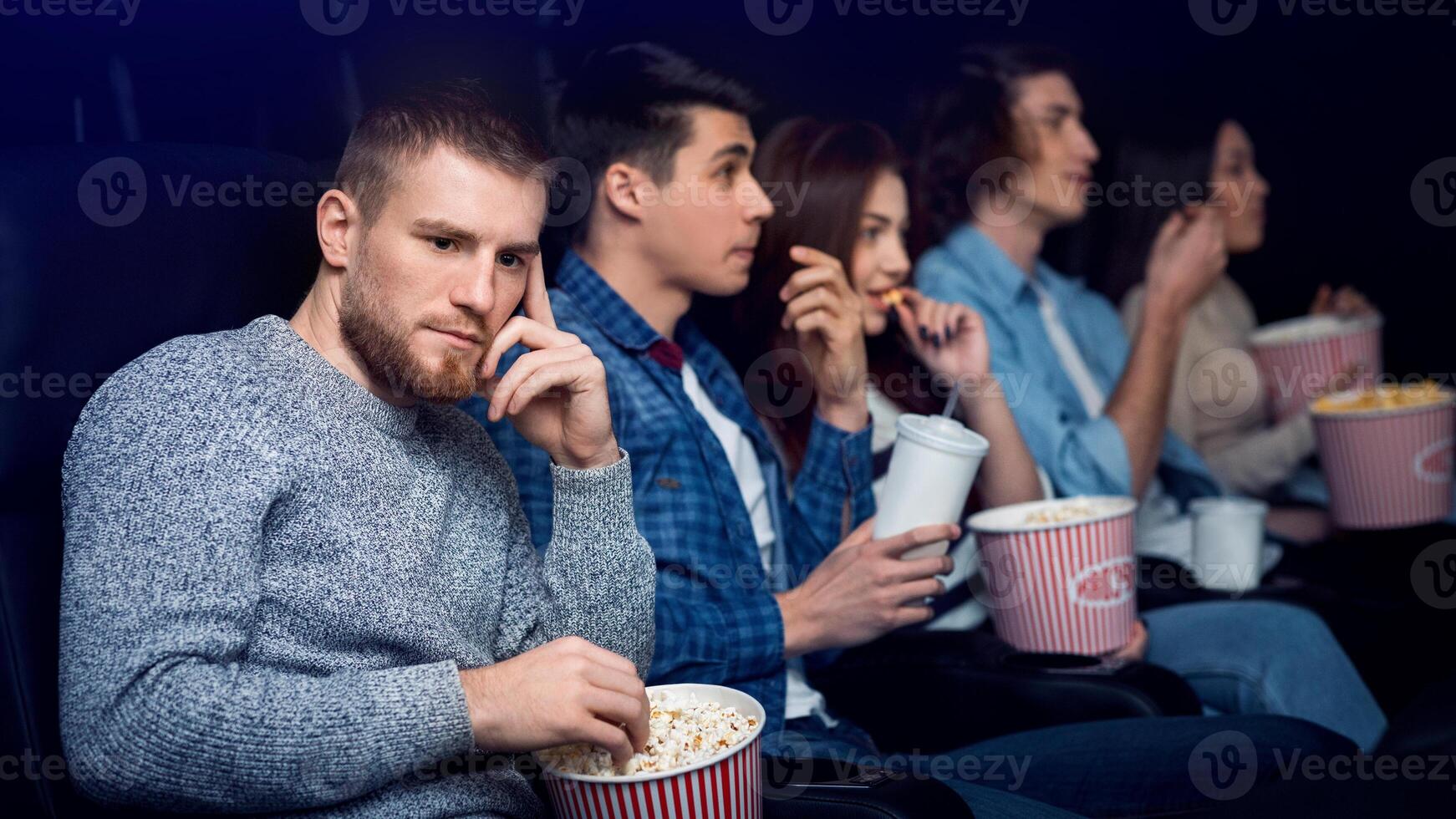 Dull movie. Bored young man with company of people in cinema photo