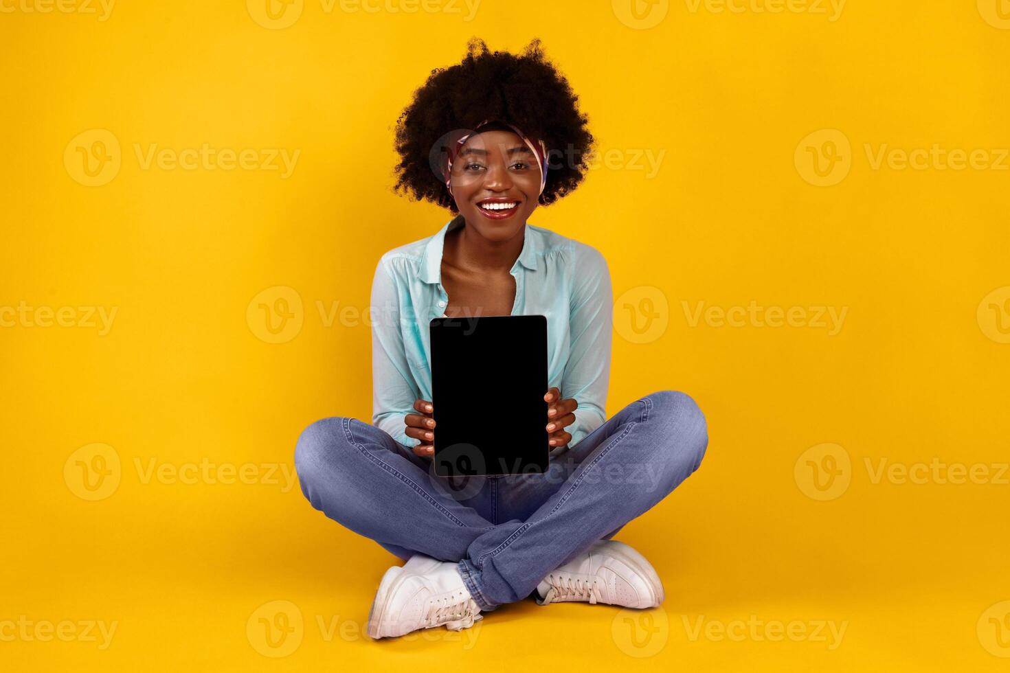 Cheerful African American Lady Showing Digital Tablet Empty Screen Sitting On Floor Posing Over Pink Studio Background, Smiling To Camera. Black Female Advertising Website Or Application. Mockup photo