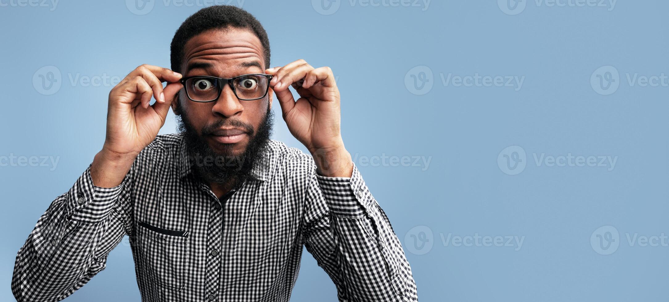 No Way. Close up headshot of surprised black man looking at camera, touching glasses, blue studio wall photo