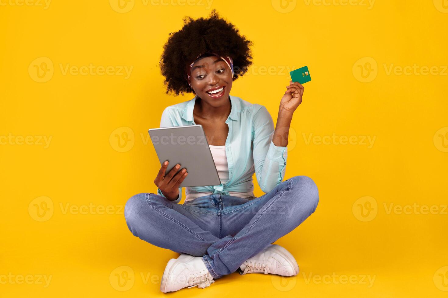Online Shopping. Happy African American Woman With Credit Card Using Digital Tablet Making Payment Sitting On Floor Over Pink Studio Background. E-Commerce, Finances Concept photo
