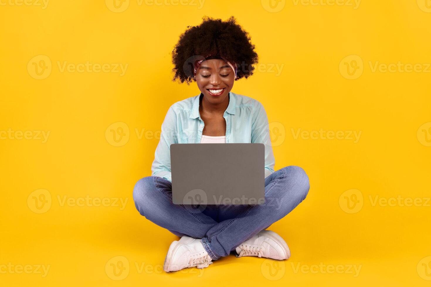 Cheerful African American Female Using Laptop Working Online And Browsing Internet Sitting On Pink Background. Black Female Typing Writing Article For Blog On Computer. E-Learning, Freelance And Distant Work photo