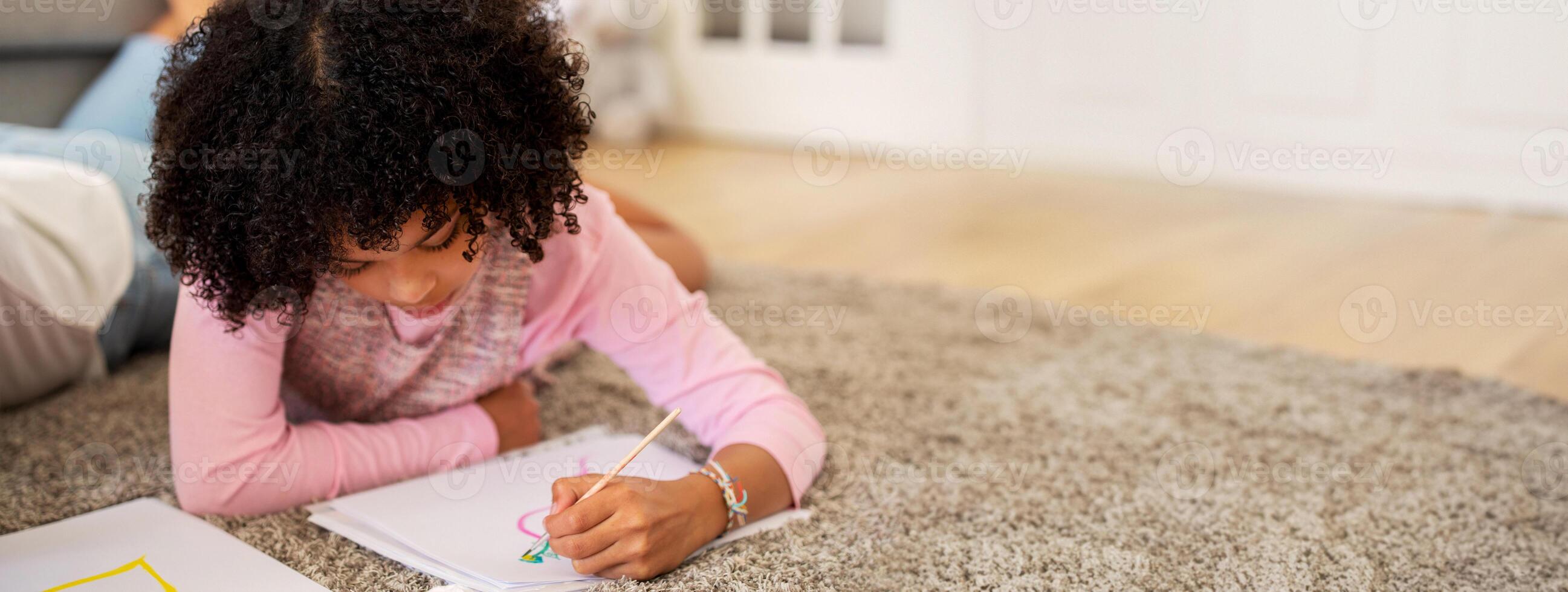 A black child enjoys her creative time by drawing colorful pictures on paper while comfortably lying on a soft carpet in her home, cherishing a quiet afternoon. photo