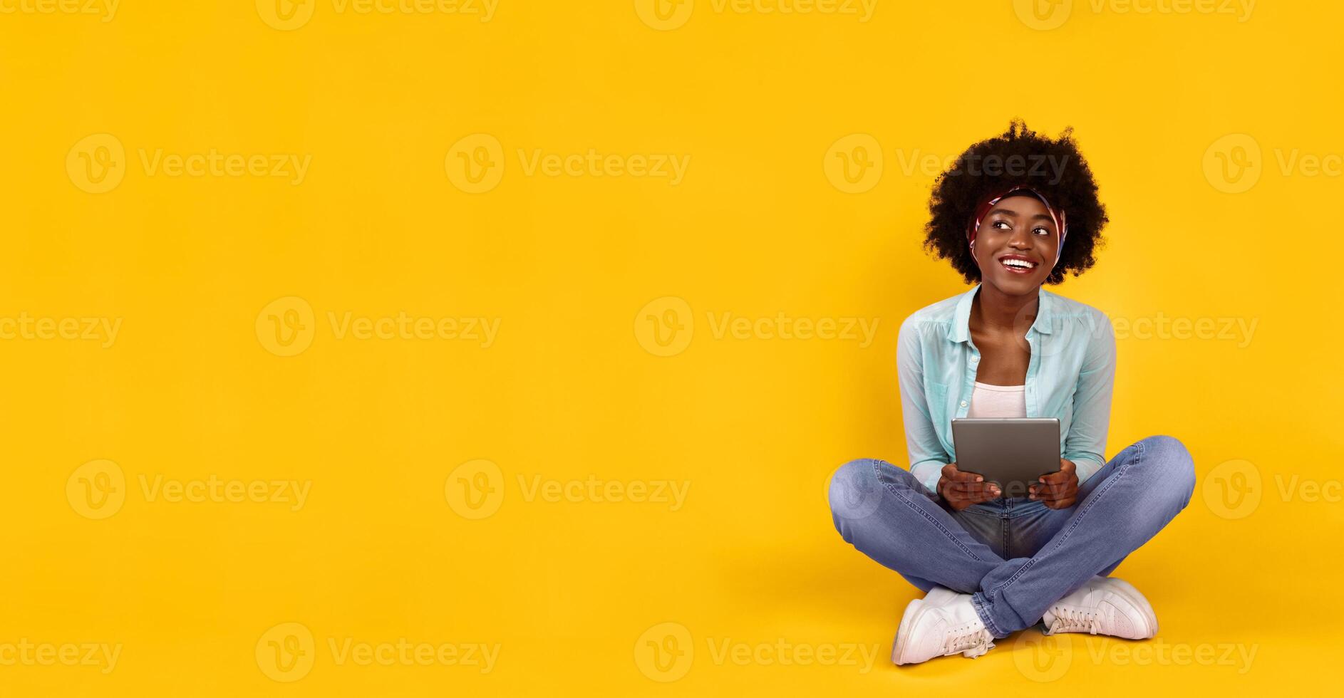 Happy Black Woman Using Digital Tablet Looking Aside At Free Space Sitting On Floor On Pink Studio Background. Bushy African Lady Posing With Computer. Gadget Lifestyle And Online Technology Concept photo