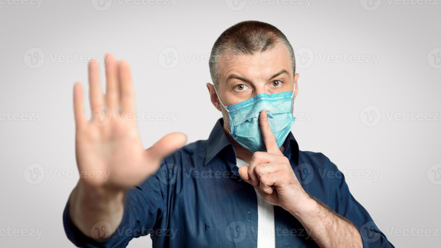 Don't Spread Panic. Man In Medical Mask Gesturing Hush Sign And Stop Gesture Over Gray Background During Pandemic. Selective Focus photo