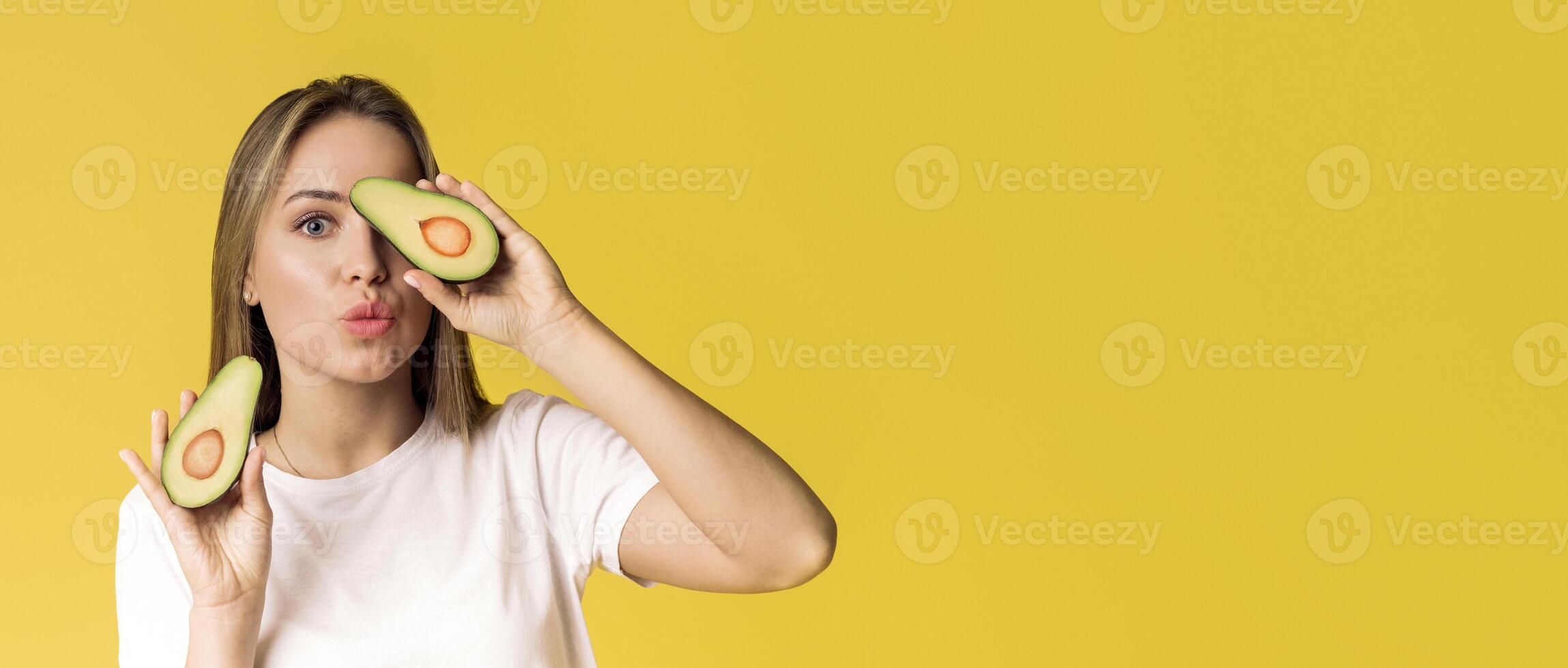 Healthy Food And Eating. Cheerful Lady Posing With Avocado Halves On Yellow Background In Studio, Empty Space photo