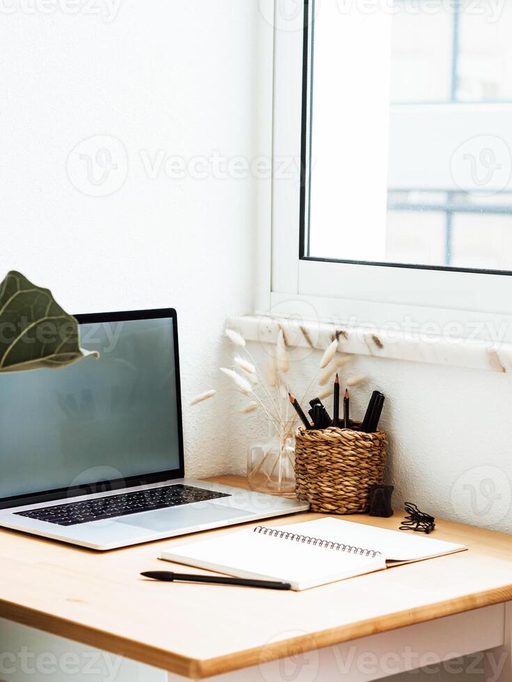 Close up view of wood table workspace with opened laptop and stationery near window in apartment photo