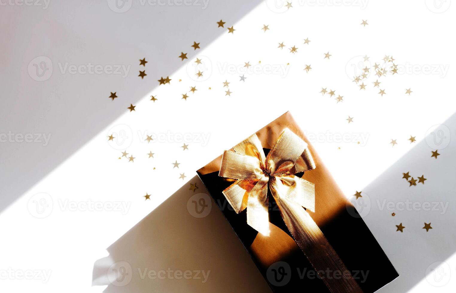 Top view Christmas gift box, adorned with vibrant golden ribbon, surrounded by golden star-shaped confetti photo