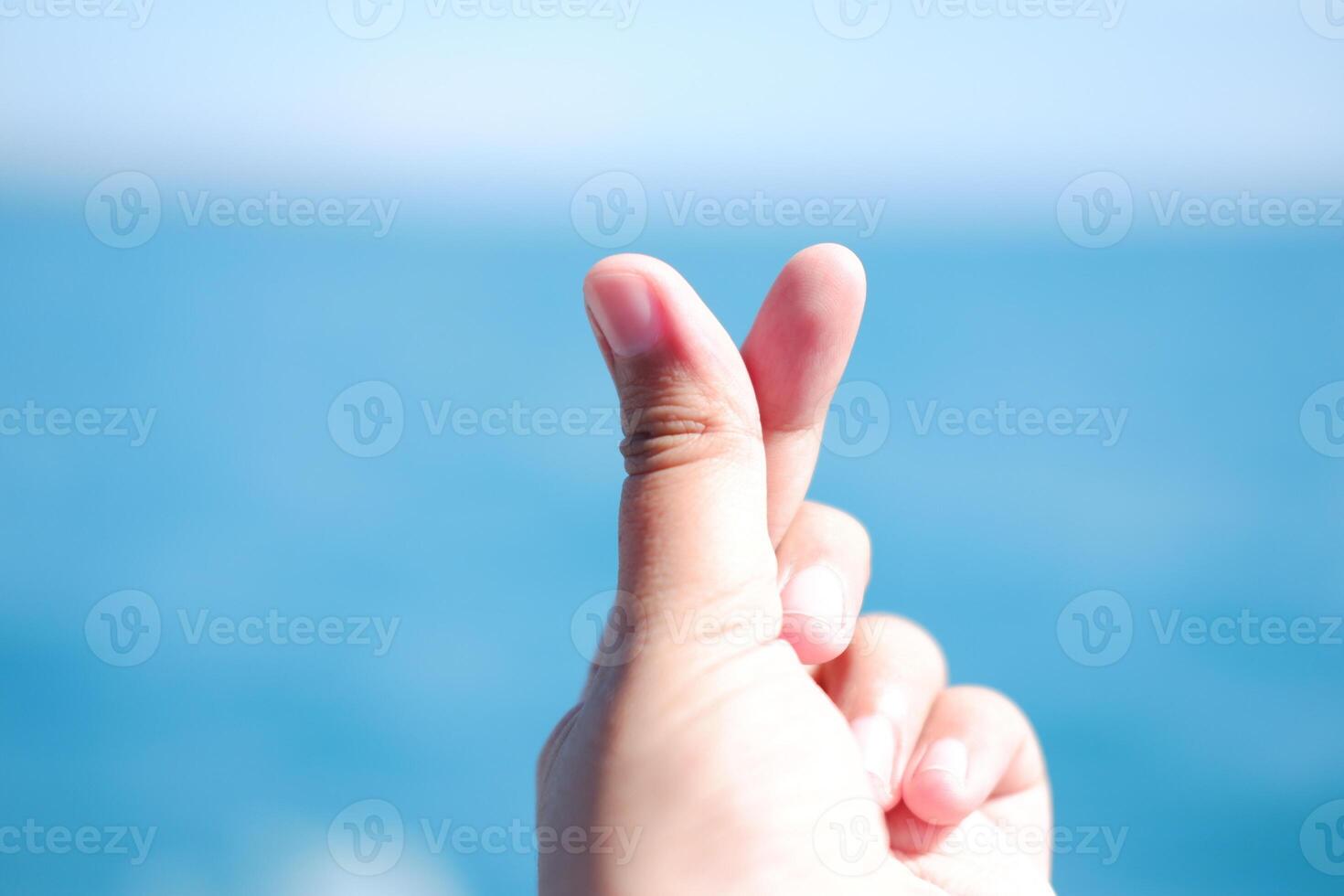 A hand making a finger heart gesture with a blurred blue background. photo