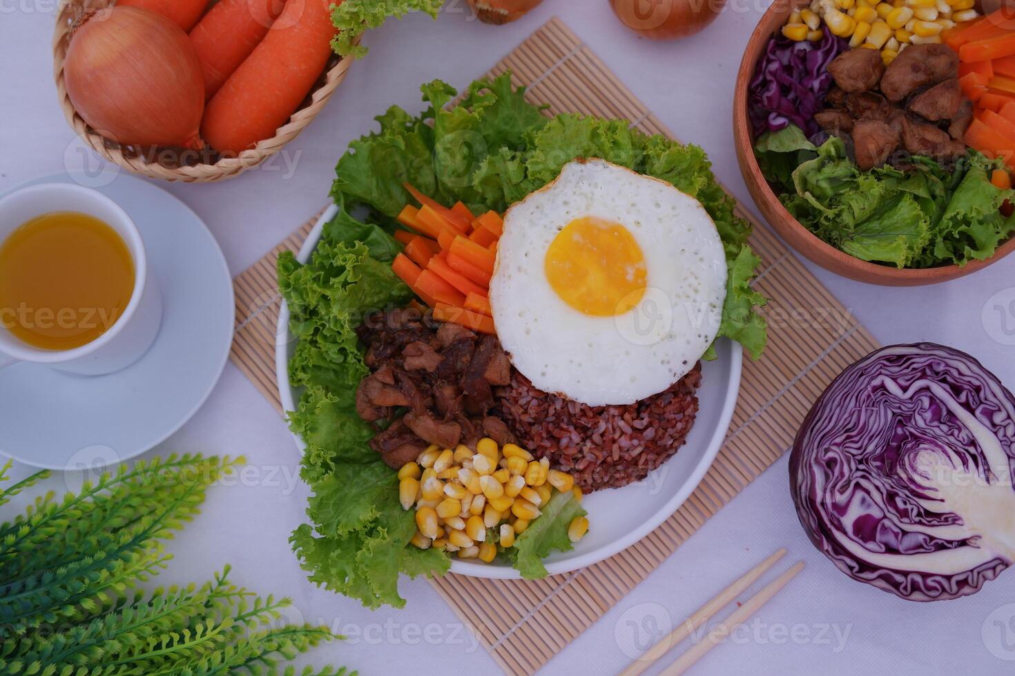 A vibrant meal consisting of red rice, meat, corn, carrots, lettuce, and a sunny side up egg photo