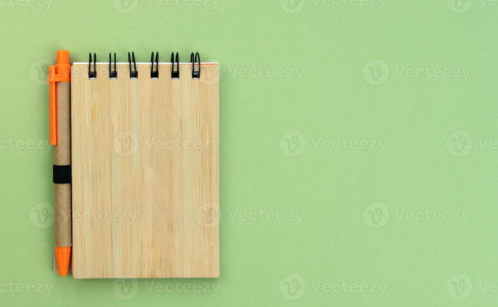 Flatlay composition with notebook and pen made of eco friendly materials on a green background. Top view. Copy space. photo