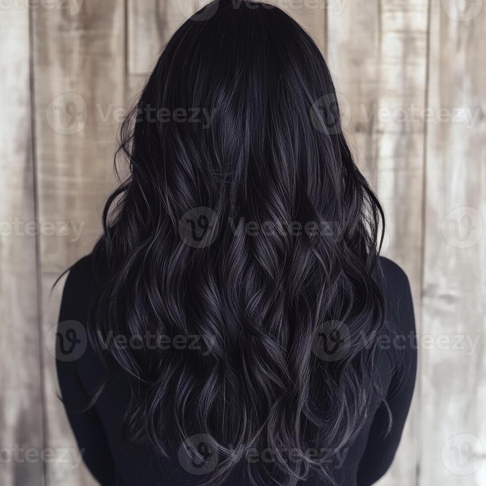 Back view of long, wavy black hair styled with soft curls, set against a rustic wooden background for a natural look. photo