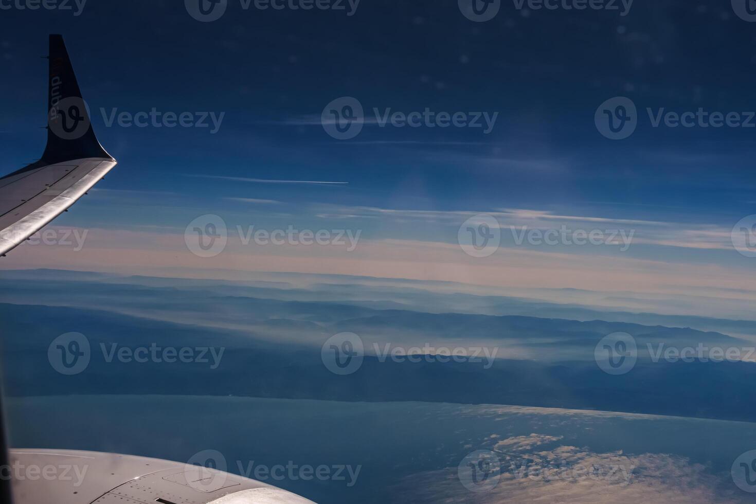 Aerial view from airplane window above green ground. View from the airplane window with beautiful clouds at sunrise. Earth and sky as seen through window of an airplane. photo