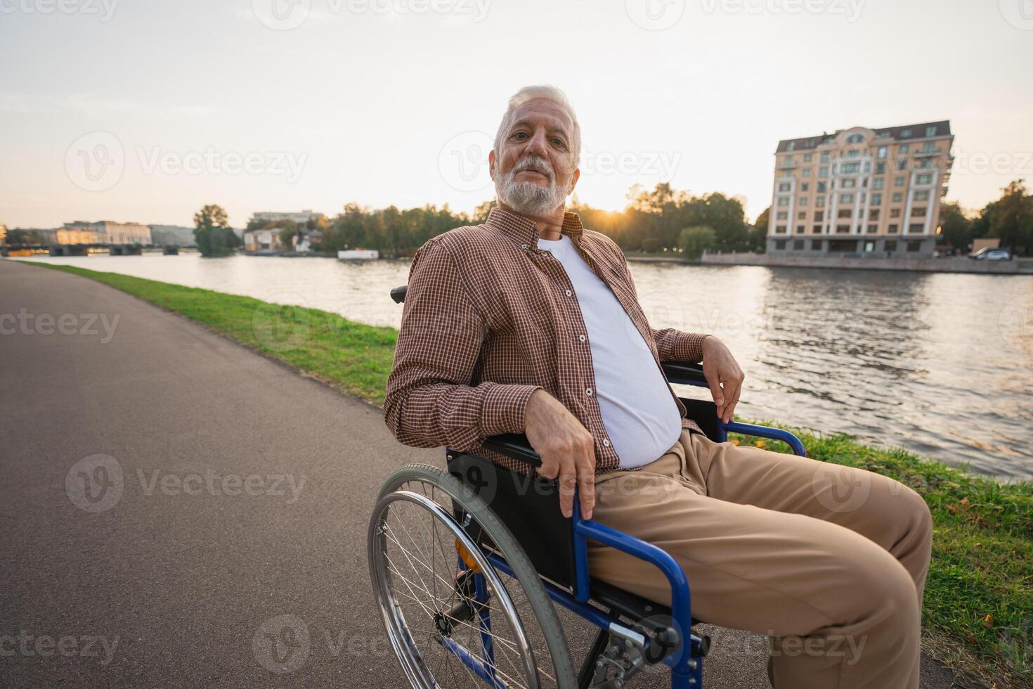 Happy senior man in wheelchair smiling enjoying freedom walking on road in city park outdoor. Old cheerful positive man in chair for people with disability. Disability disease rehabilitation photo