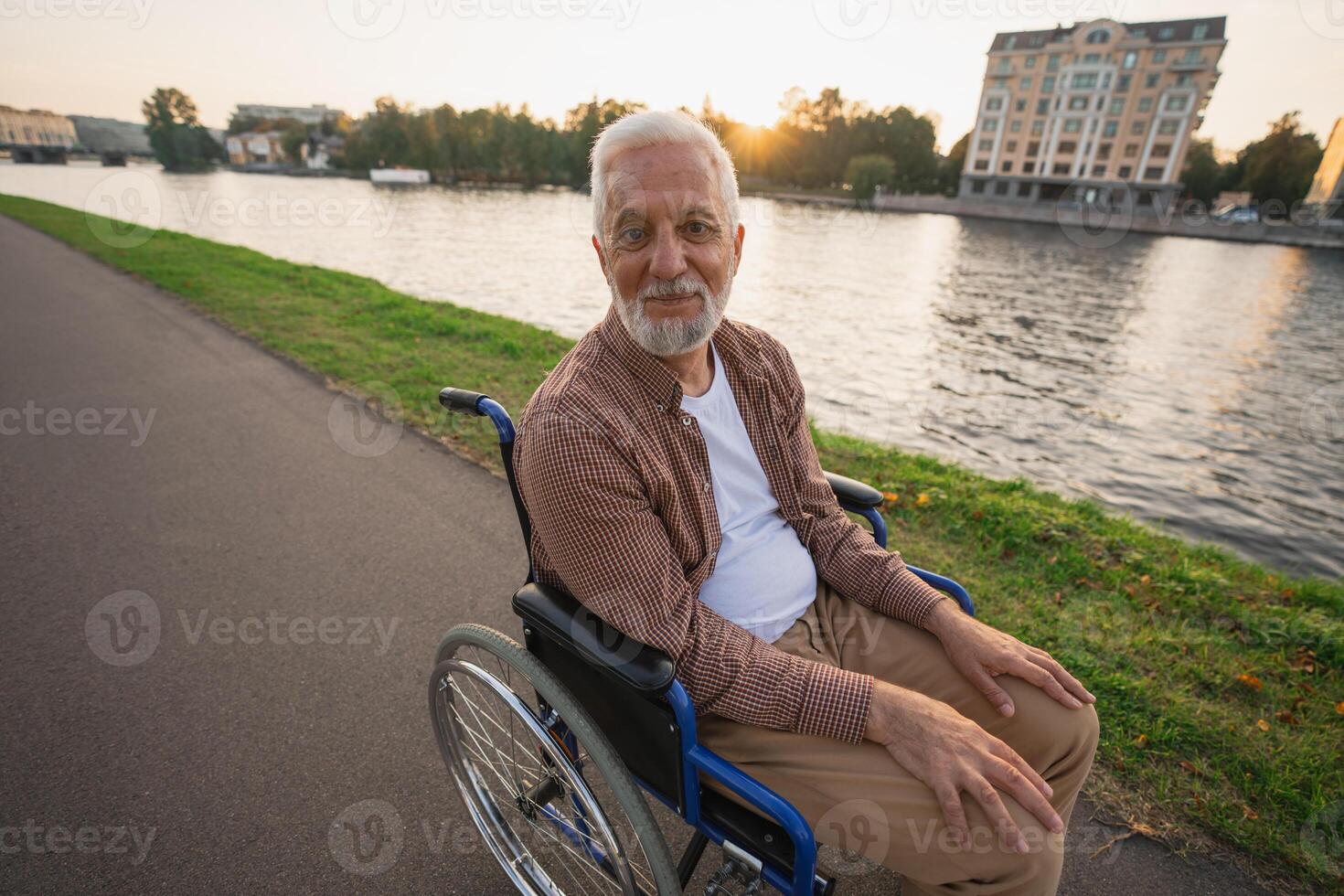 Happy senior man in wheelchair smiling enjoying freedom walking on road in city park outdoor. Old cheerful positive man in chair for people with disability. Disability disease rehabilitation photo