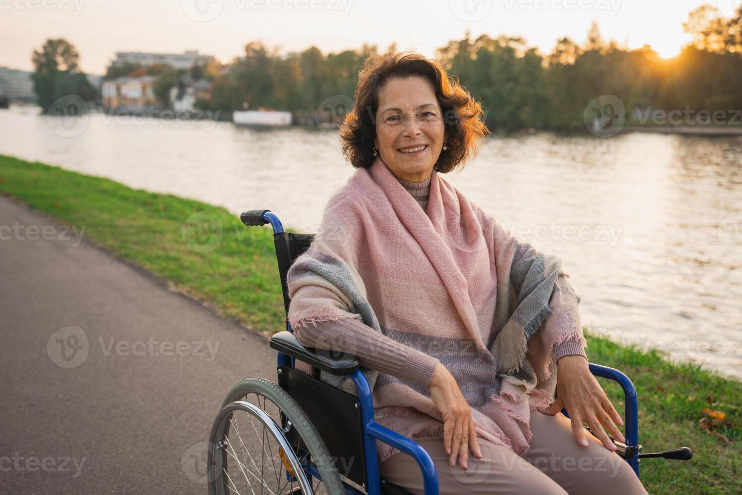 Happy senior woman in wheelchair smiling enjoying freedom walking on road in city park outdoor. Old cheerful positive woman in chair for people with disability. Disability disease rehabilitation photo