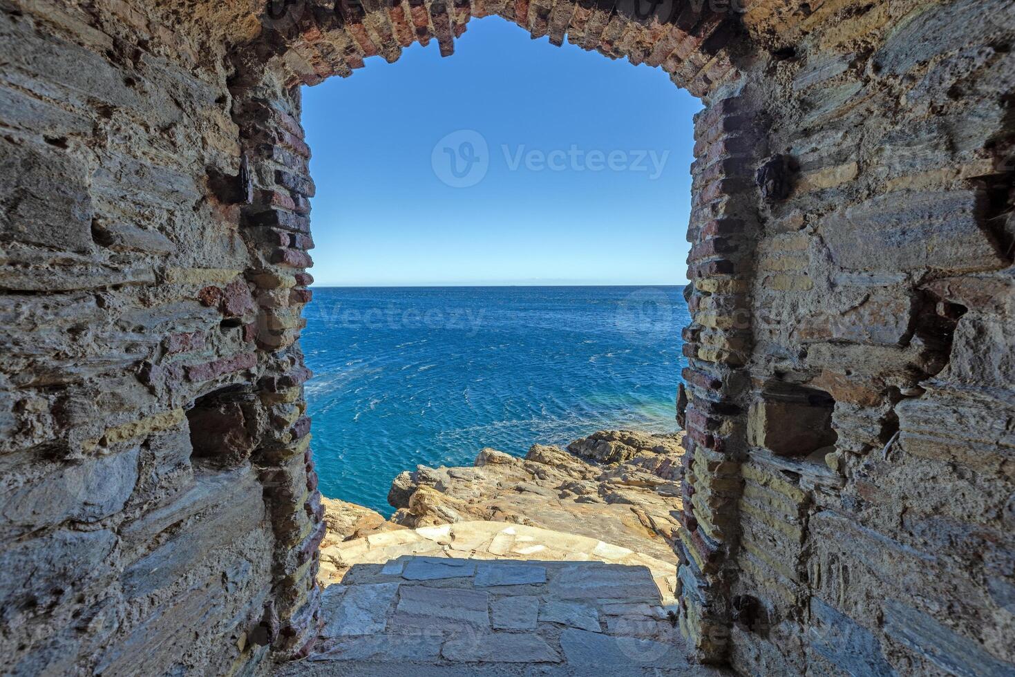 View through an ancient stone archway leading to the rugged coastline and the open sea photo