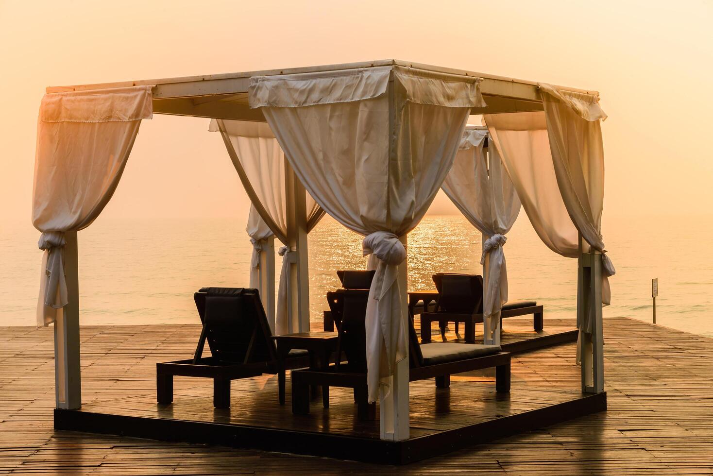 A gazebo with white curtains on the beach at sunset photo