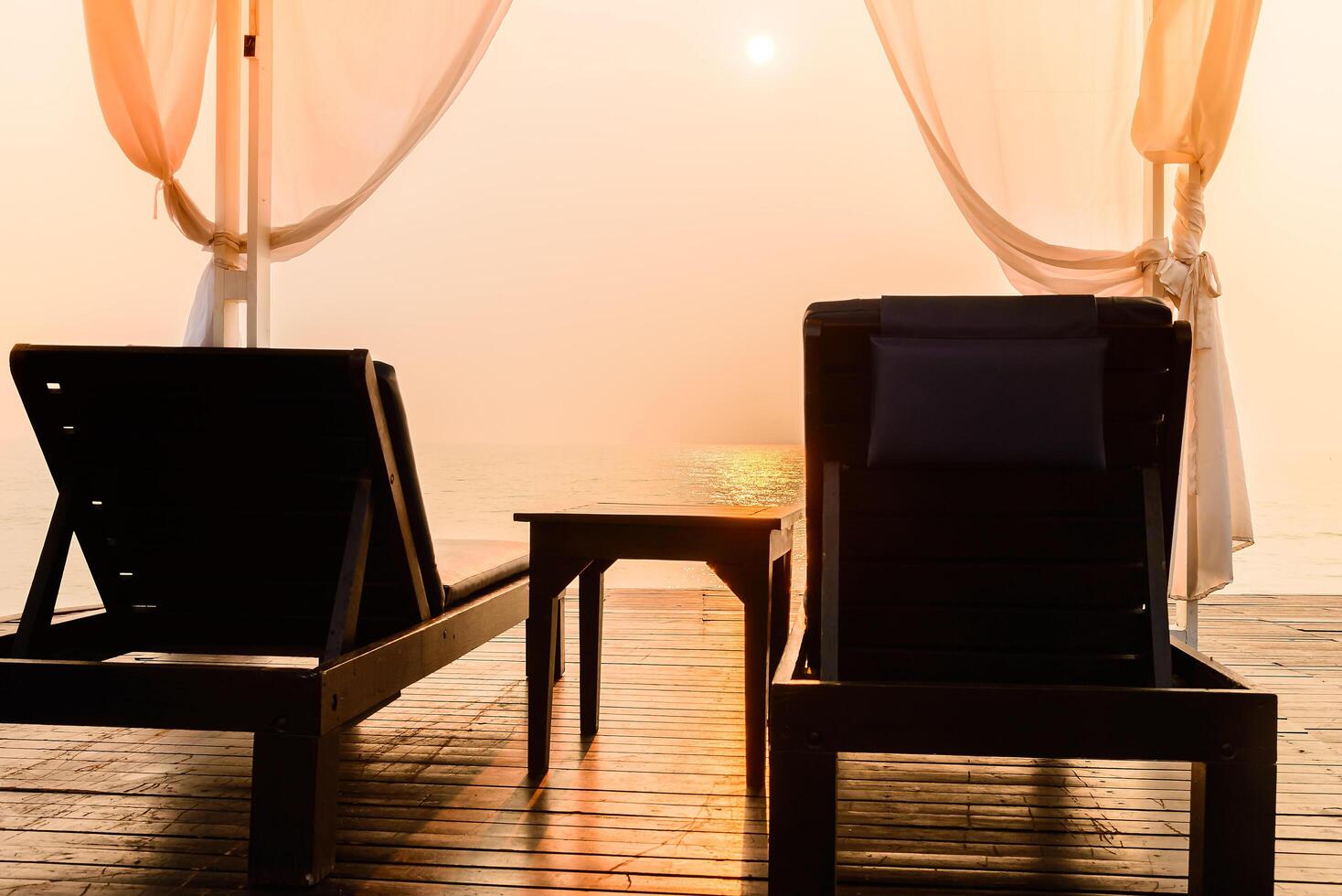 Two chairs sit on a wooden deck overlooking the ocean photo