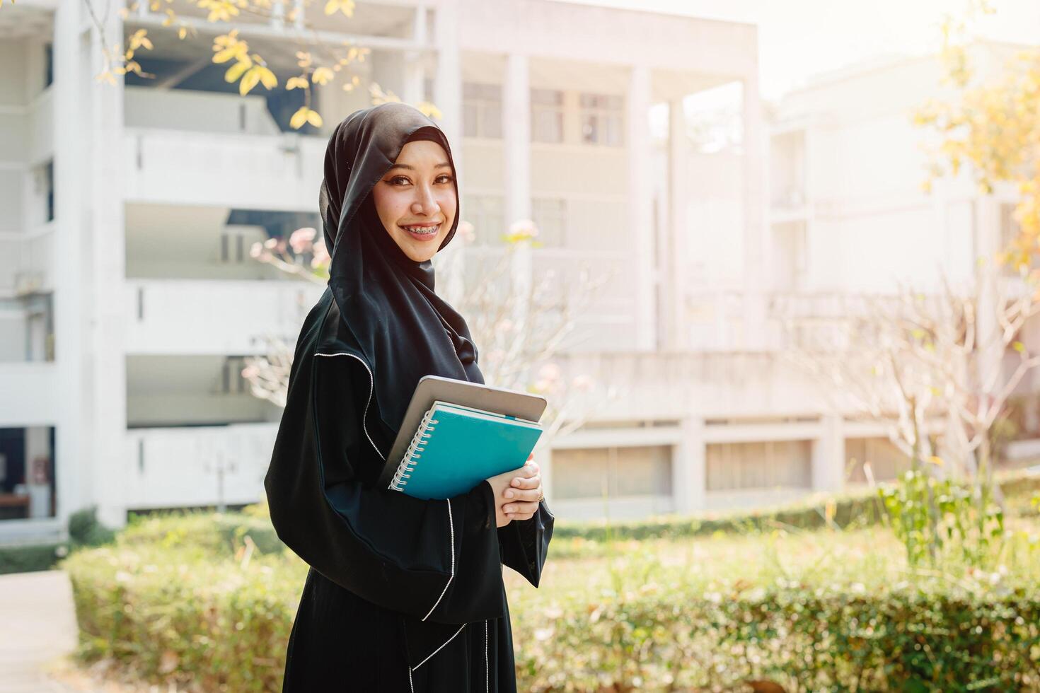 University saudi muslim niqab woman high education in university campus happy smiling with modern knowledge book. Arab saudi black chador lady. photo