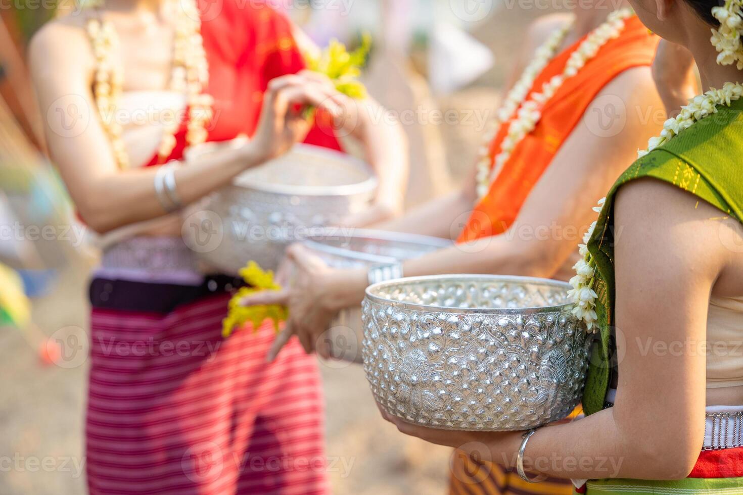 Songkran festival. Closeup Thai people in Traditional clothes dressing in Songkran day hand holding handcraft silver bowl carrying water splashing together in summer. photo