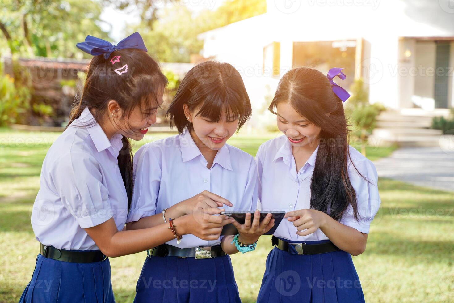 Group of Thai students looking a social network on tablet at school lawn with sun bright background. photo