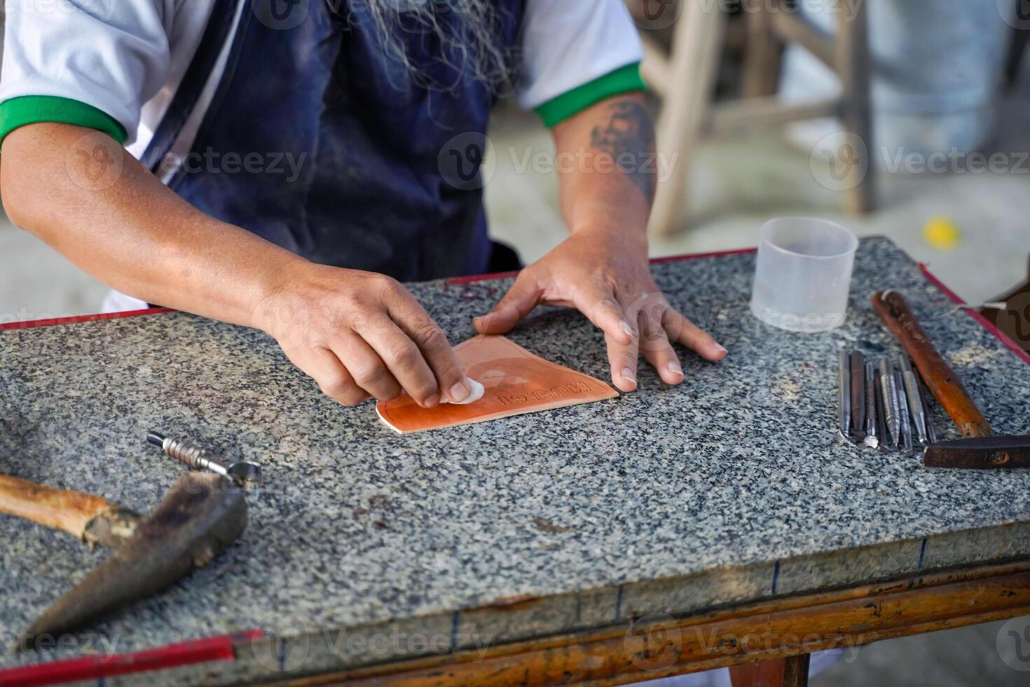 Closeup hands of leather craftsman is carefully to use a cotton swab soaked in water to wipe the leather sheet to make it soft for easy stamping design. photo