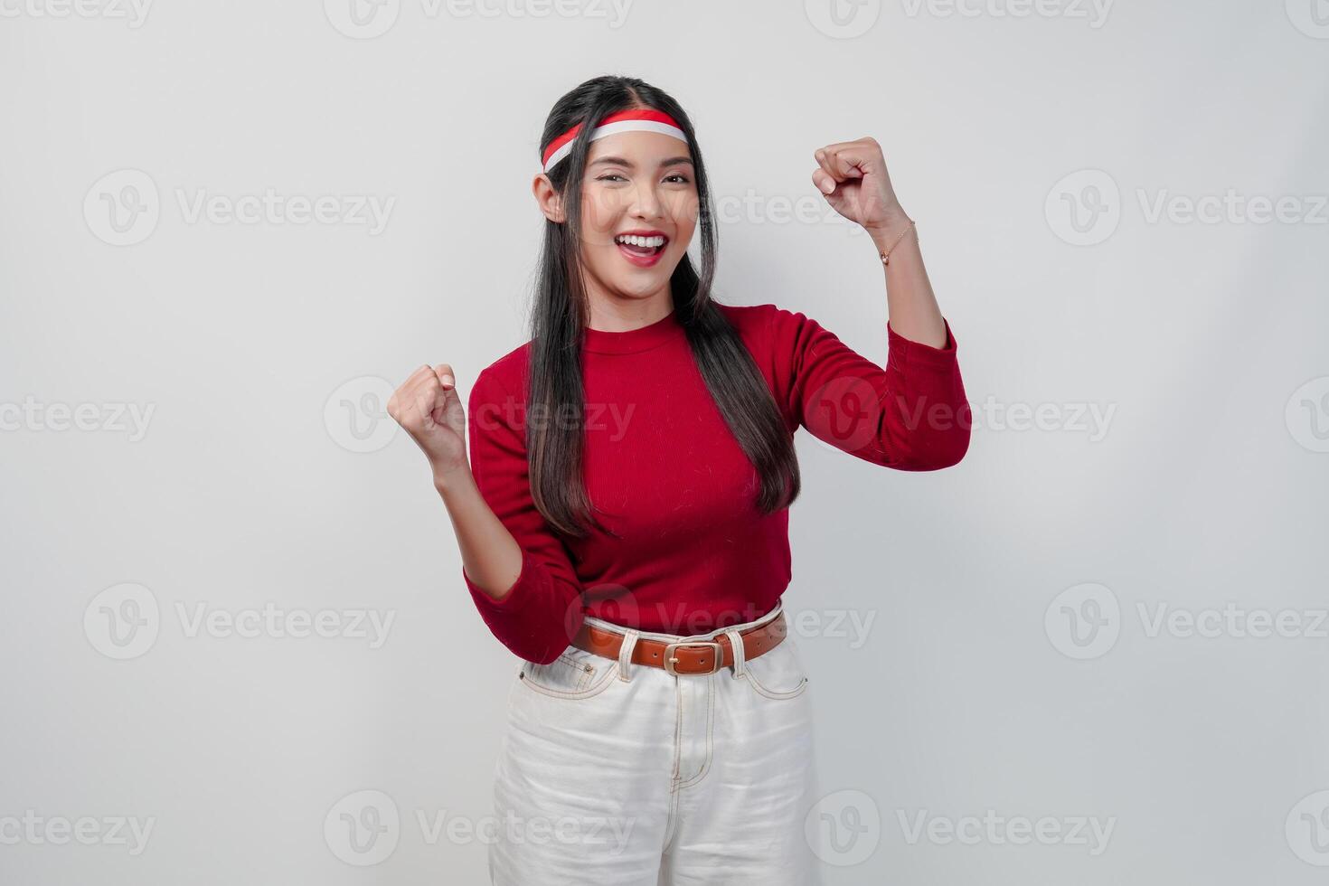 Excited young Asian woman in a red shirt and white pants is raising her hands. photo