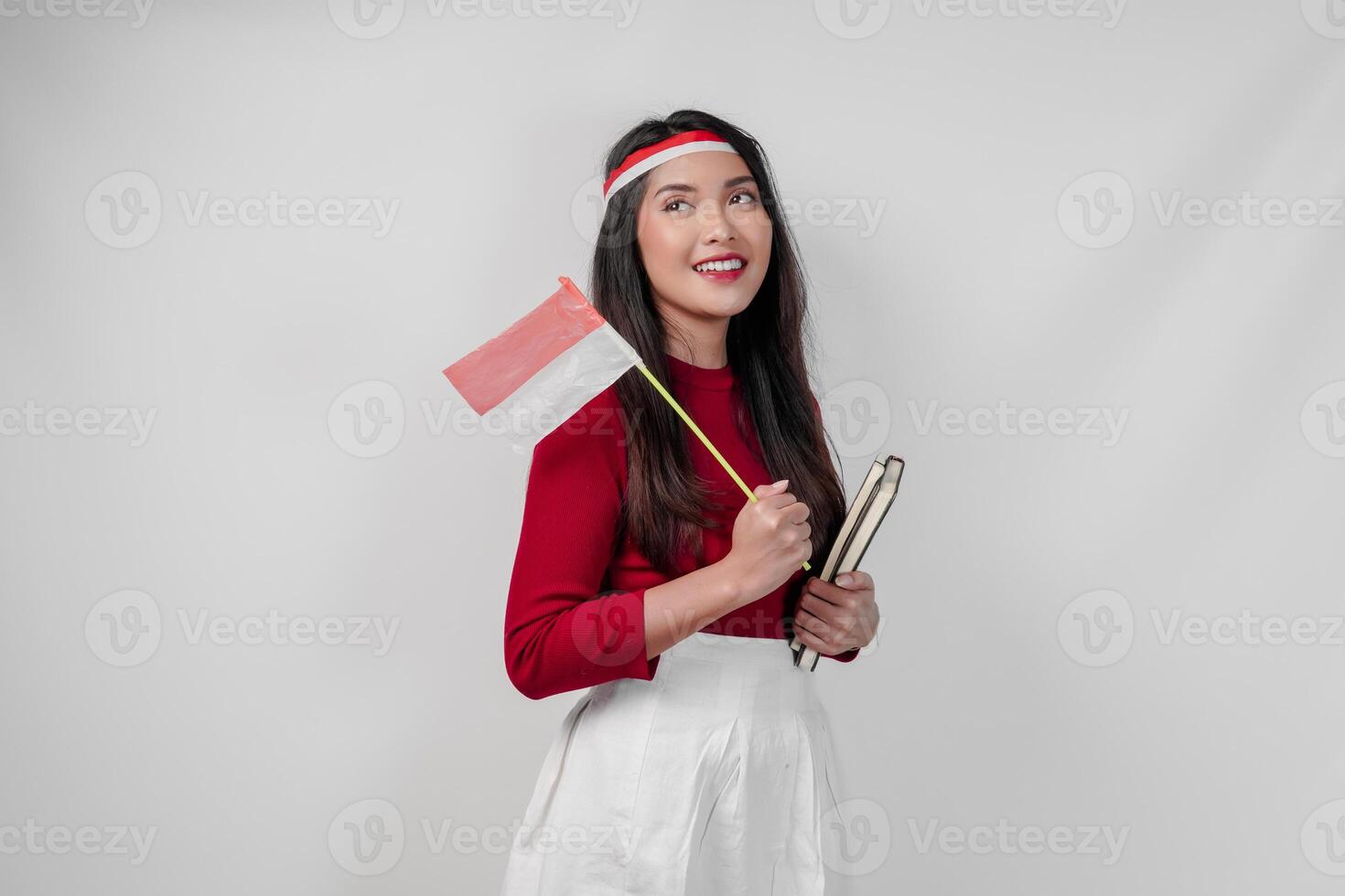 Cute young Asian woman wearing holding a mini country flag and a book, smiling to the camera. photo