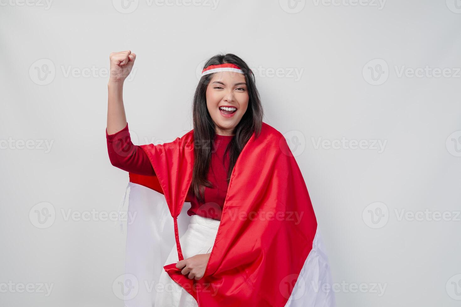Happy young Asian woman with Indonesia flag draped over her shoulders and raising fist hand gesture. photo