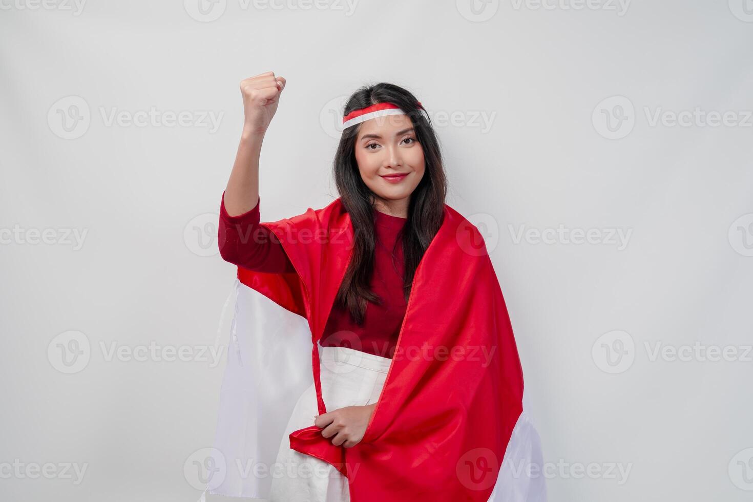 Happy young Asian woman with Indonesia flag draped over her shoulders and raising fist hand gesture. photo