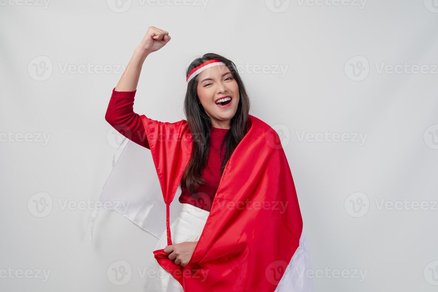 Happy young Asian woman with Indonesia flag draped over her shoulders and raising fist hand gesture. photo