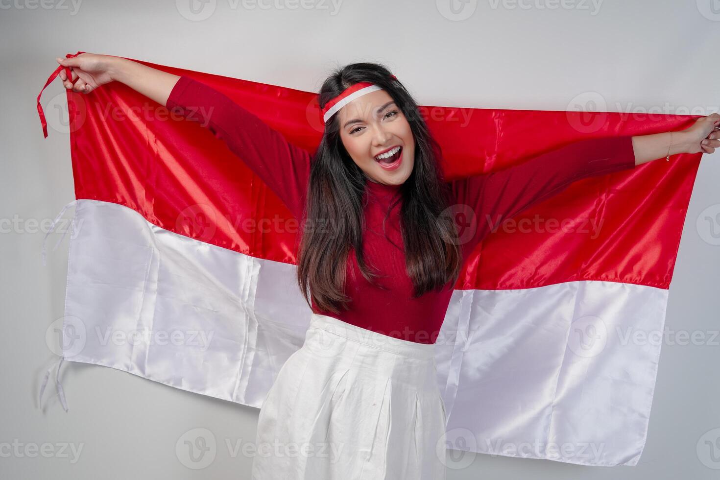 Excited young Asian woman is spreading Indonesian flag at her back and smiling. photo