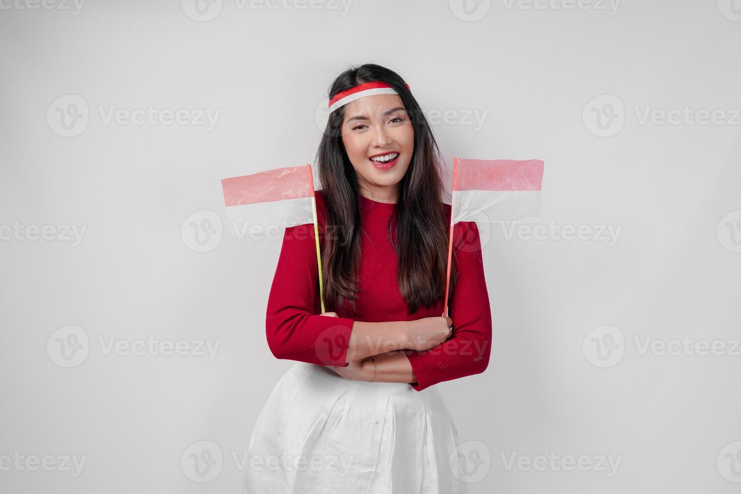 Happy young Asian woman is holding two mini Indonesian flags and smiling with crossed arms gesture. photo