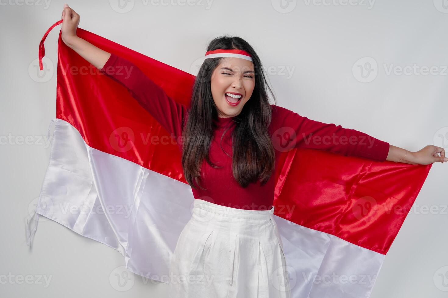Excited young Asian woman is spreading Indonesian flag at her back and smiling. photo