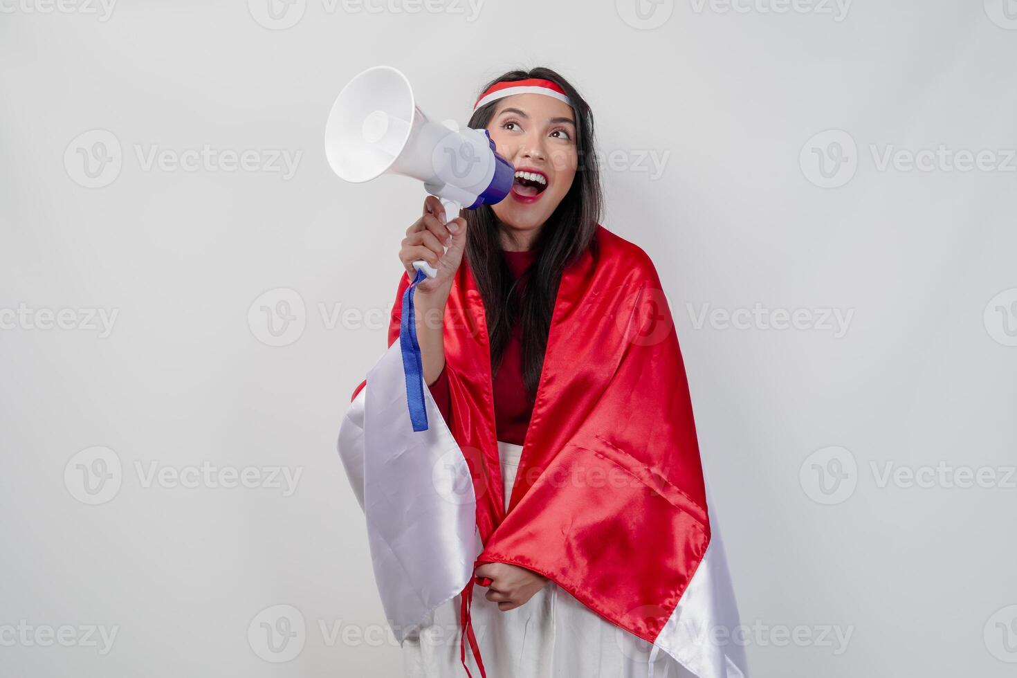 Energetic Asian woman with country flag draped over her shoulder while shouting at a megaphone. photo