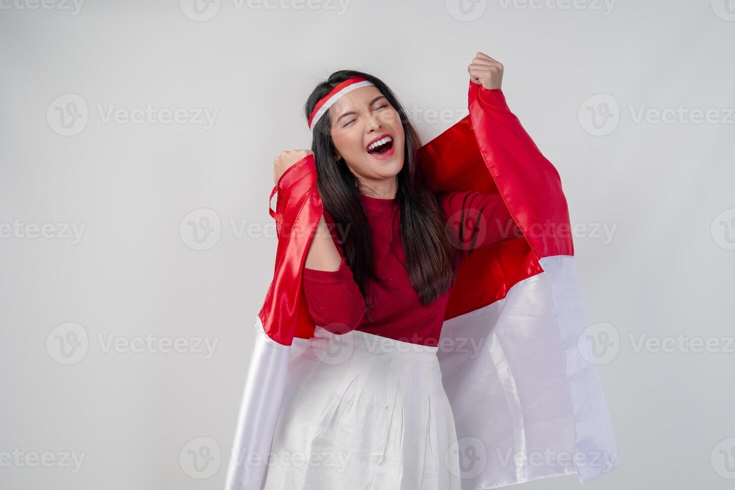 Cheerful young Asian woman is holding Indonesian flag at her back and raising fists. photo