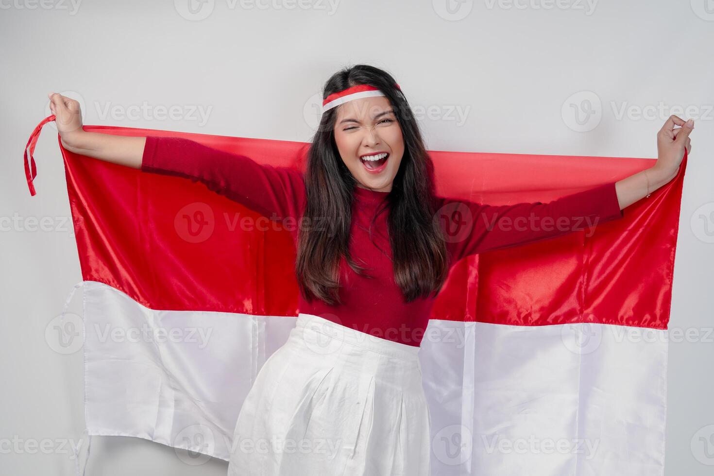 Excited young Asian woman is spreading Indonesian flag at her back and smiling. photo