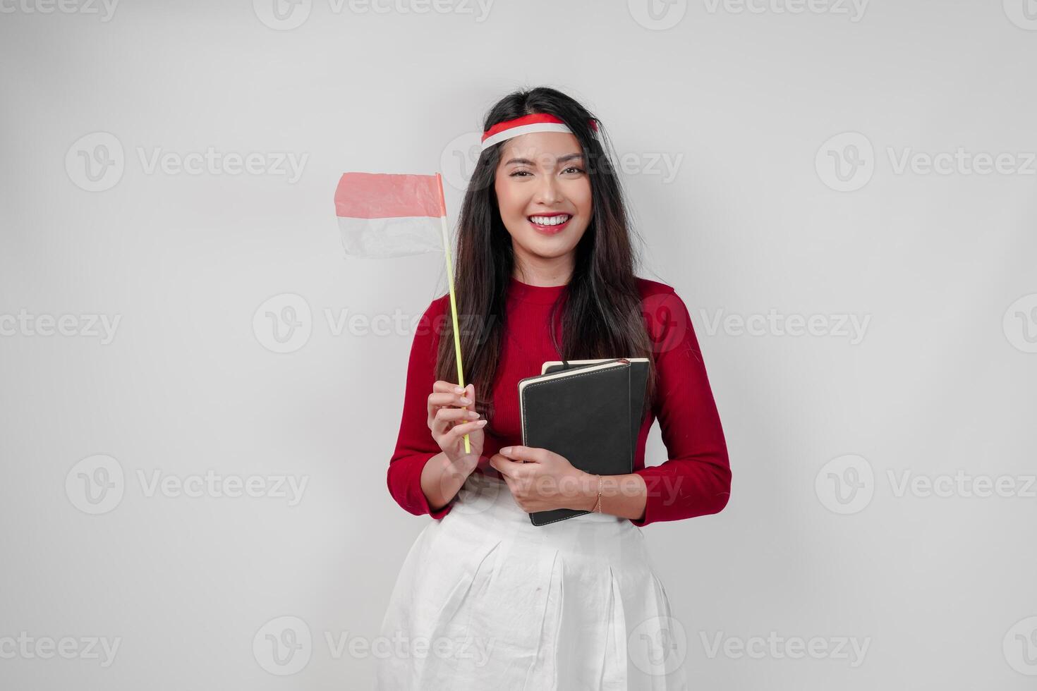 Cute young Asian woman wearing holding a mini country flag and a book, smiling to the camera. photo