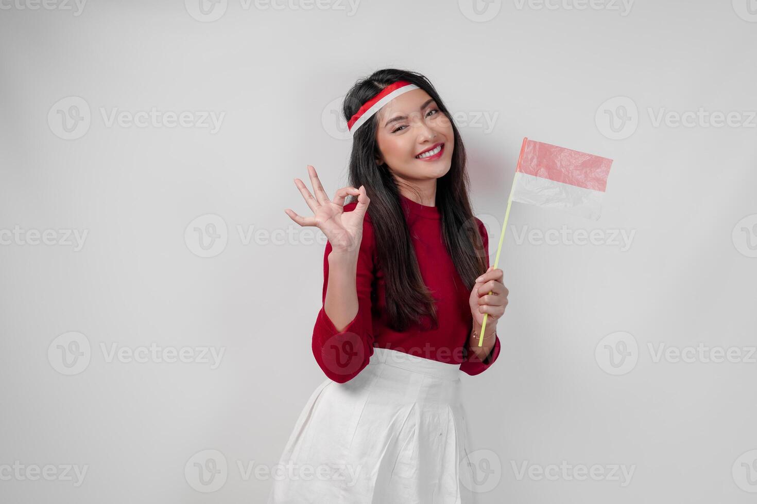 Beautiful young Asian woman is giving okay hand gesture while holding mini country flag. photo