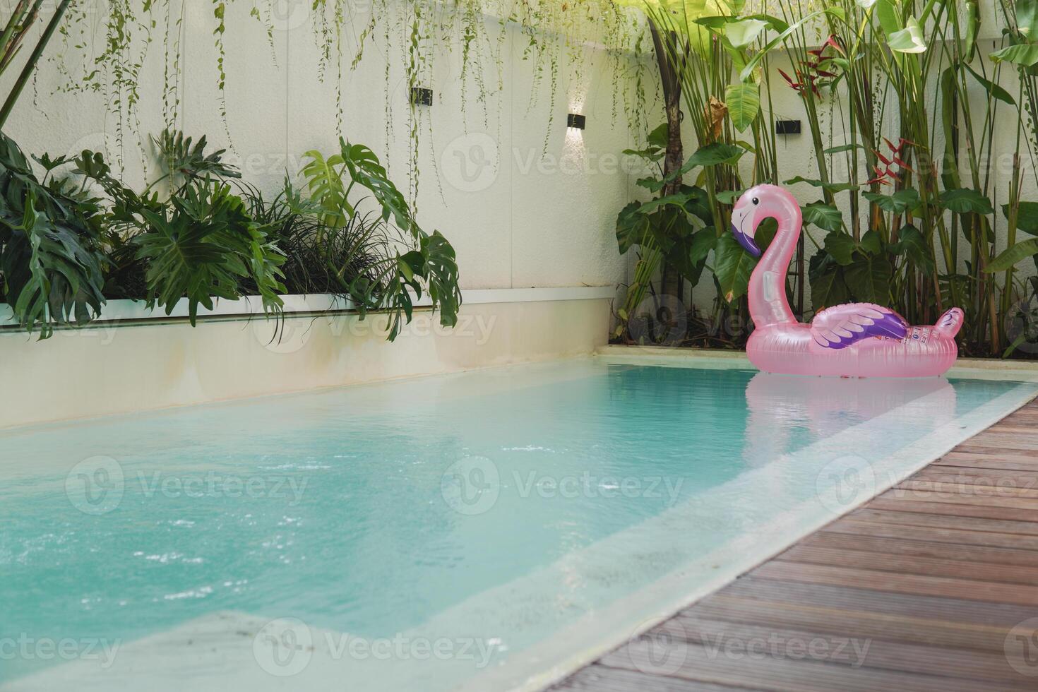 A pink inflatable flamingo floats in a pool. The pool is in a backyard, and there are two lounge chairs on the deck. photo