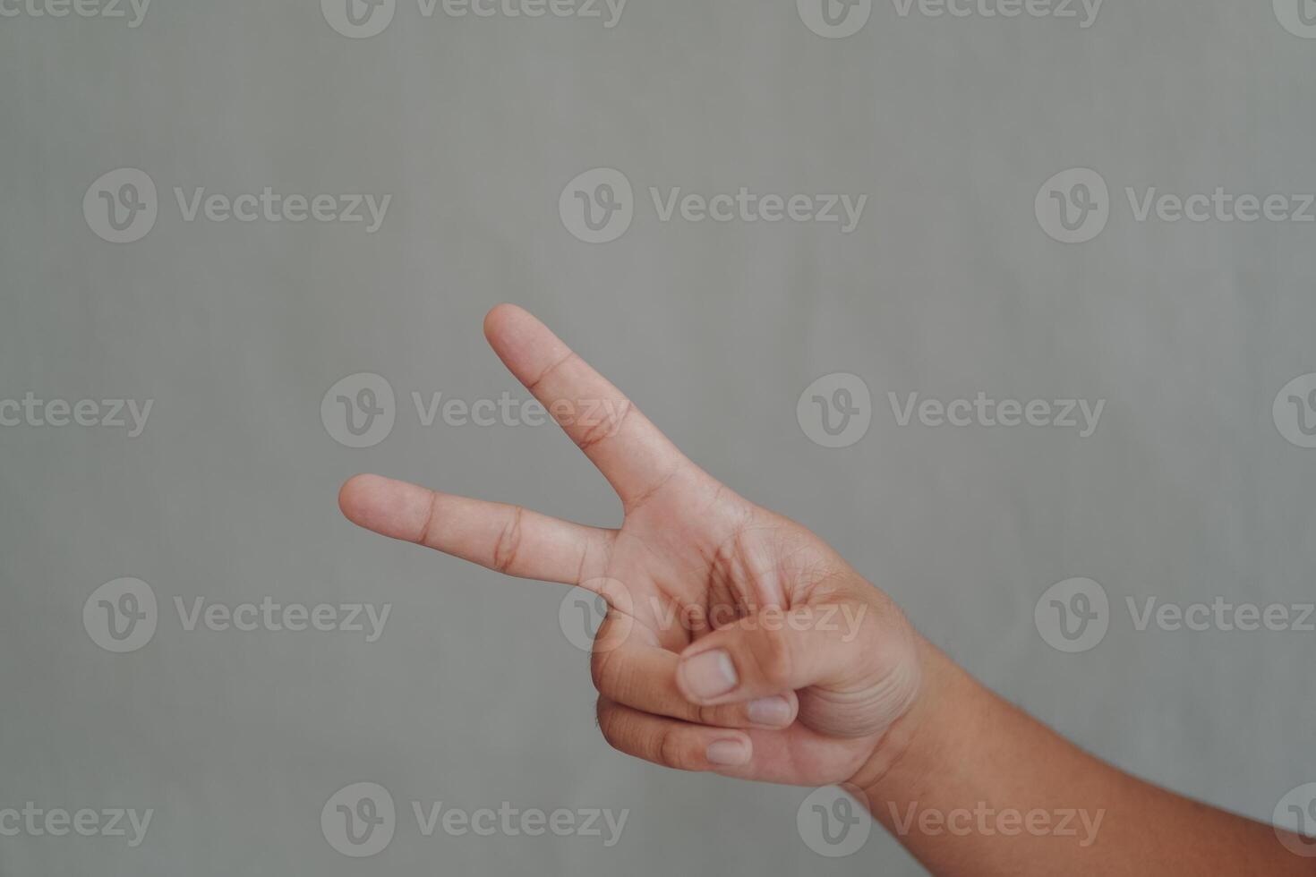 A hand is holding up two fingers, which is a symbol of peace, isolated over grey background. photo