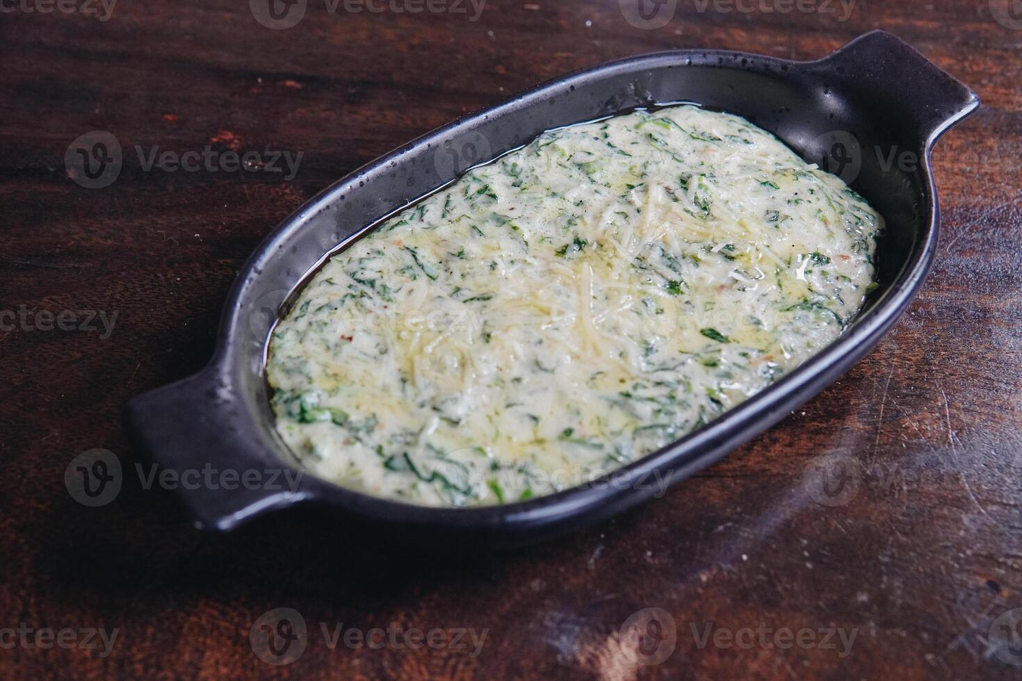 Delicious creamy spinach in a black bowl looks appetizing and inviting served on a wooden table. photo