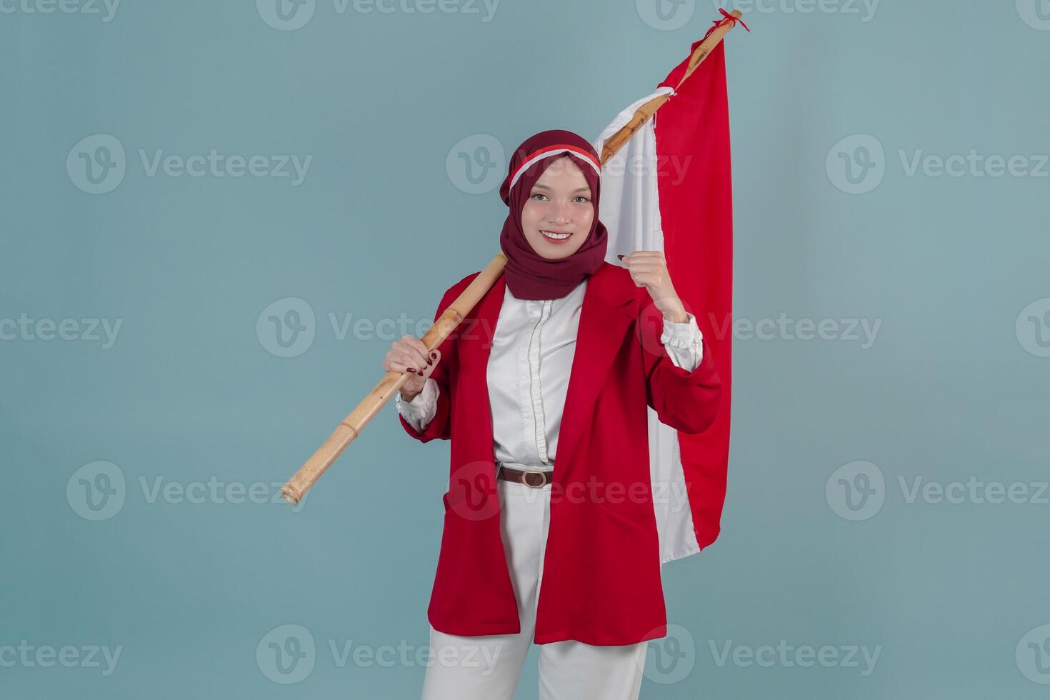 Confident Indonesian woman wearing a red jacket holding a flag while raising fist gesture. photo