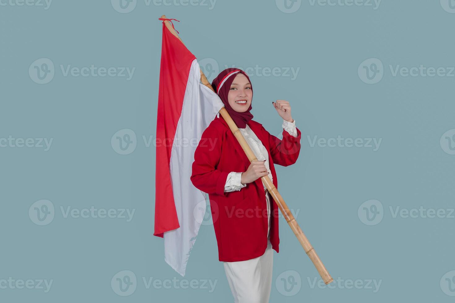 Smiling Indonesian woman wearing a red jacket is holding a flag while raising fist gesture. photo