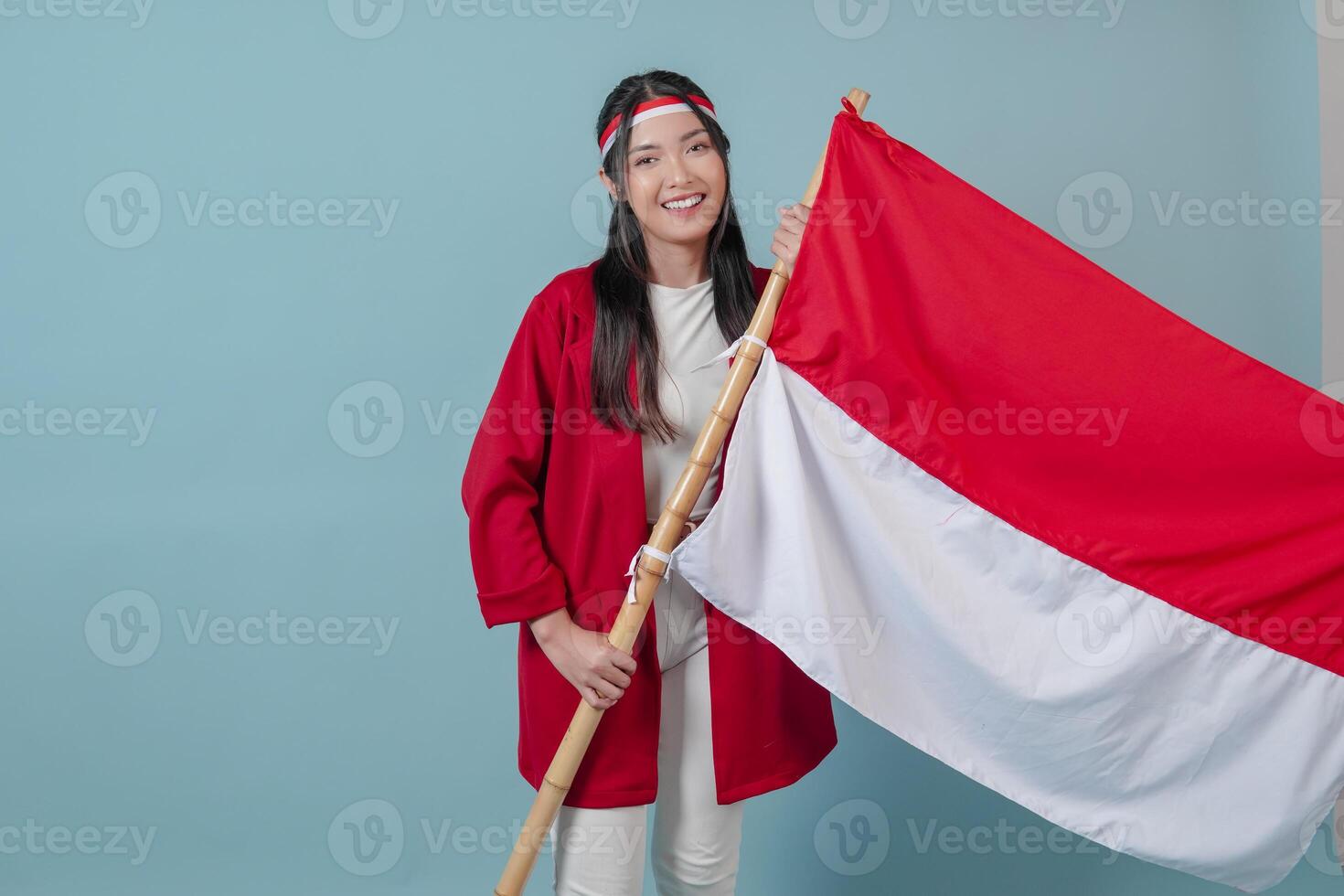 Proud Indonesian woman holding country flag, standing over isolated blue background. photo