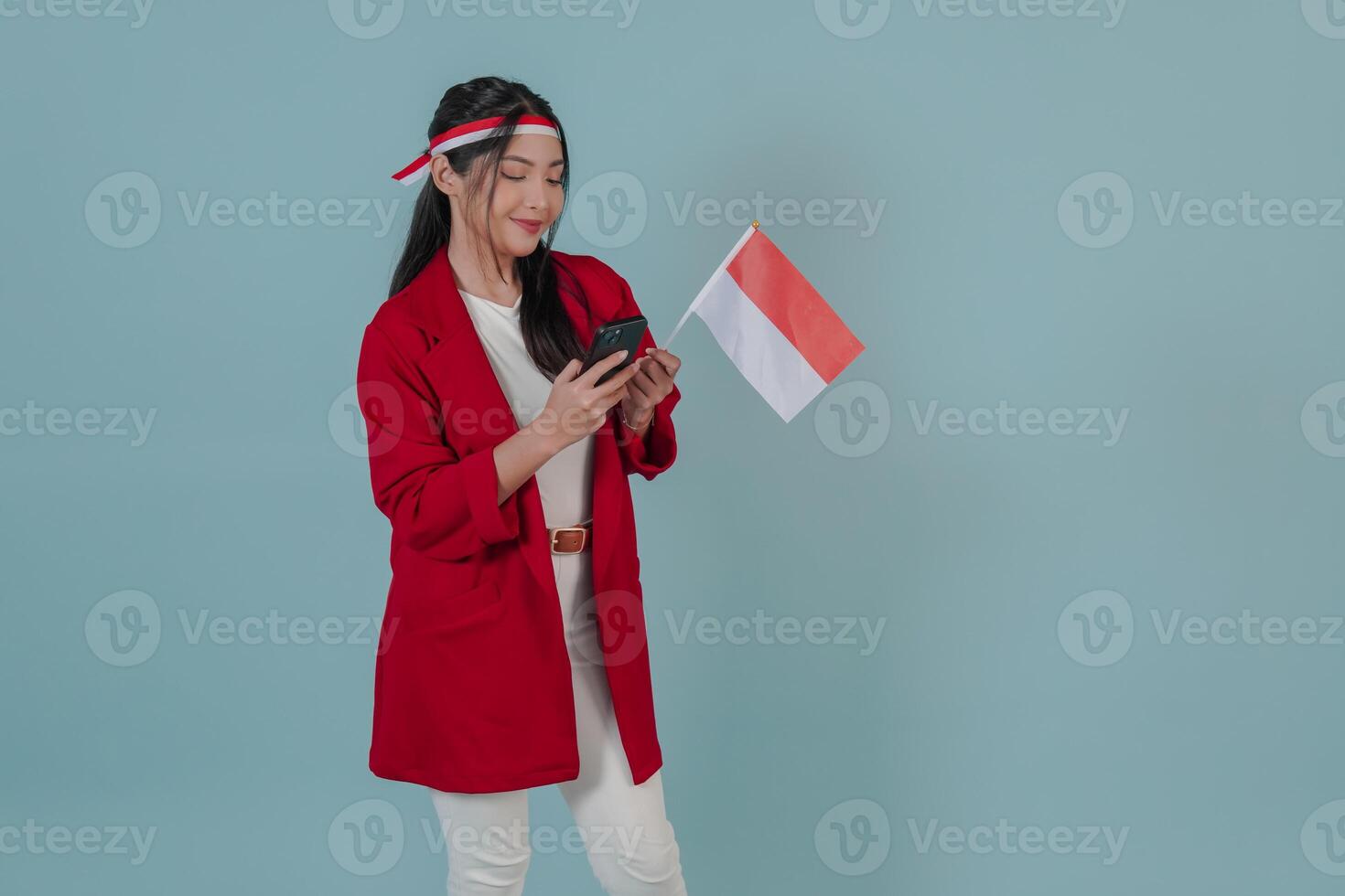 Happy Indonesian young woman holding a flag while using smartphone to browse internet. photo