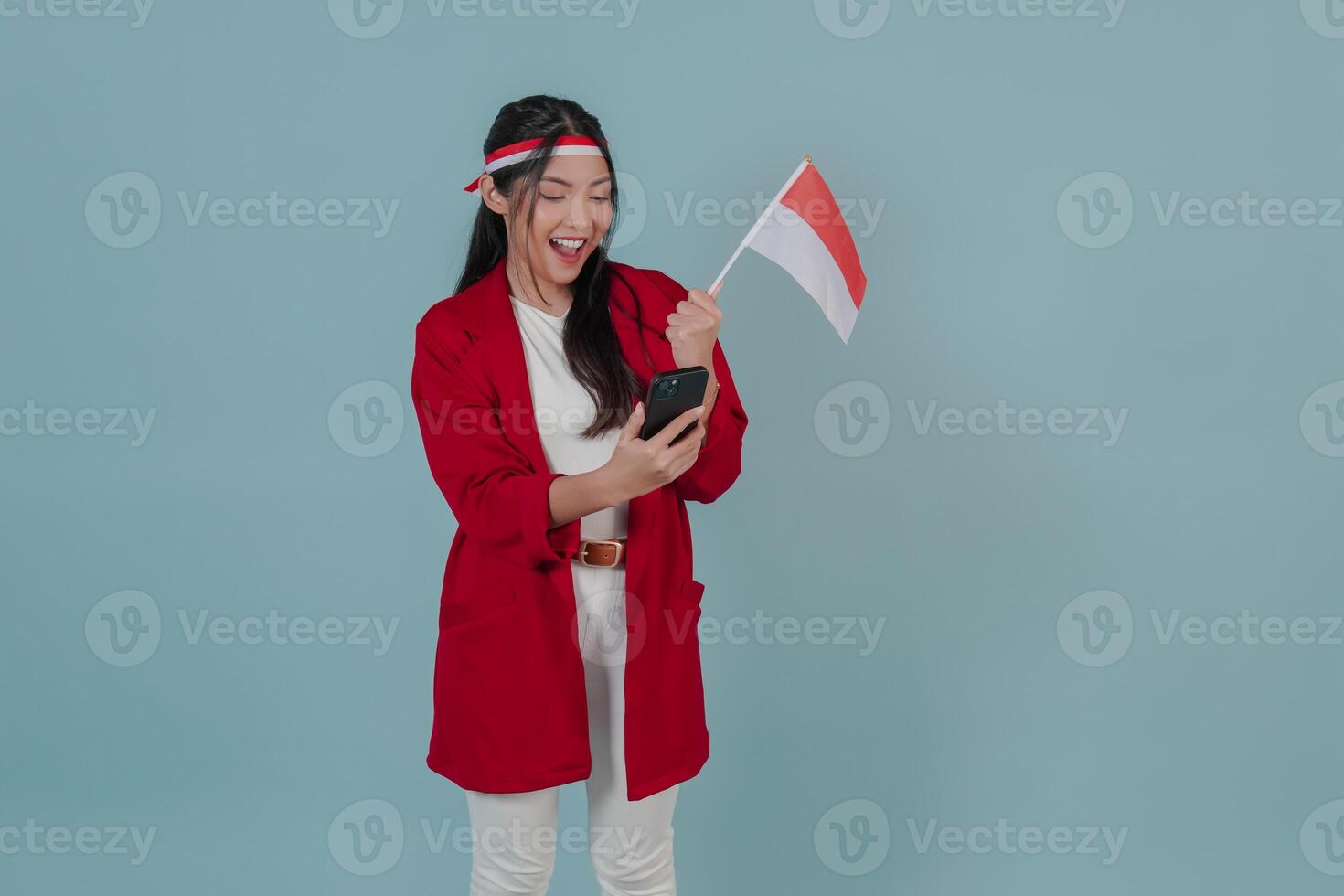 Excited Indonesian young woman holding a flag while using smartphone to browse internet. photo