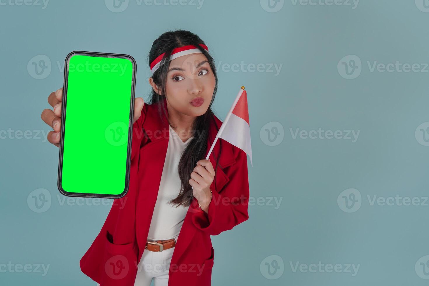 Young Indonesian woman holding a mini country flag while presenting copy space on her phone screen. photo