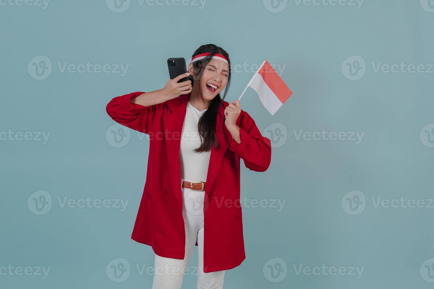 Excited young Indonesian woman holding mini flag and smartphone with happy successful expression. photo