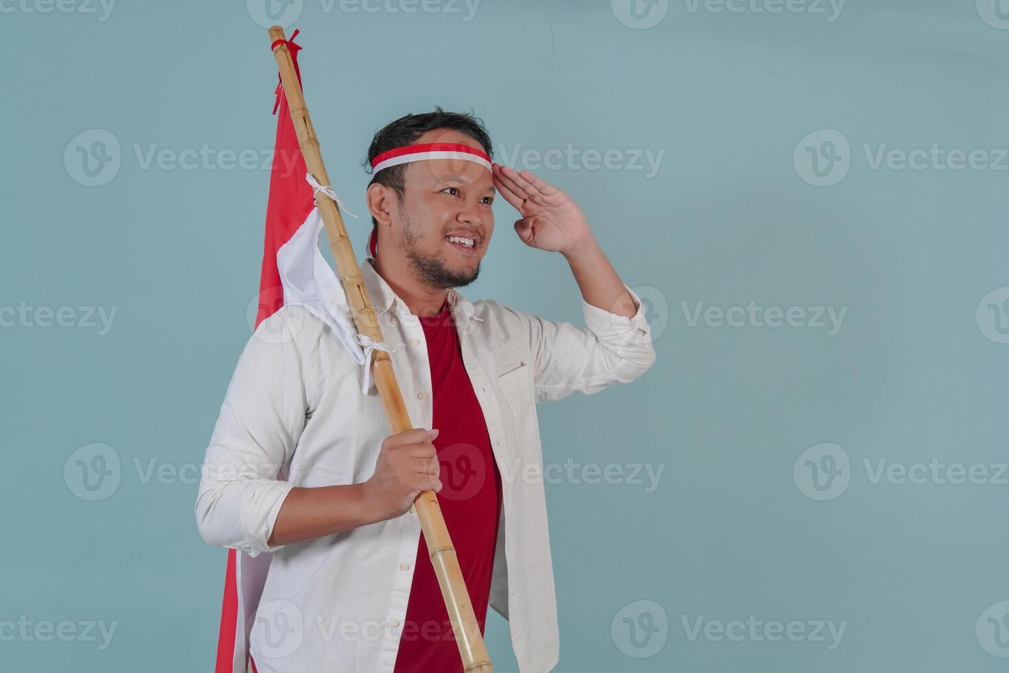 Happy Indonesian man is holding country flag while doing salute gesture. photo